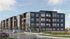 Modern four-story apartment complex with contemporary design, featuring large windows and welcoming greenery in an urban setting.