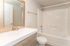 Bright and modern bathroom featuring a sleek vanity, large mirror, and pristine bathtub with white tile surround.