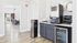 Modern apartment amenity space featuring a sleek coffee station with a high-tech machine, stylish cabinetry, and a cozy lounge area visible in the background.