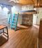 Cozy room with a stylish loft bed, exposed brick wall, wooden flooring, and natural light. Features a turquoise ladder and modern lighting.