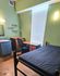 Cozy bedroom with green walls, featuring a single bed, study desk, ergonomic chair, and built-in sink, perfect for a serene living space.