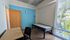Bright minimalist room featuring a single bed, large window with blinds, blue accent wall, and a spacious desk.
