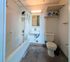 Bright bathroom with modern fixtures, featuring a bathtub with shower, sleek white sink, and convenient shelving for storage.
