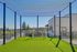 Inviting rooftop mini soccer field with netted enclosure, lush green turf, and a panoramic city view, perfect for active living.