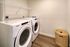 Modern laundry room featuring a sleek washer and dryer with ample shelving and elegant wooden flooring.