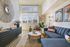 Chic modern living room with plush blue sofa, stylish decor, and large sunlit windows.