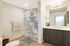 Bright and elegant bathroom with chic wooden cabinetry, dual sink vanity, and serene shower curtain. Modern lighting complements the sleek design.