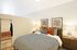 Elegant bedroom with stylish decor, featuring a cozy bed with patterned upholstery, warm lighting, and modern artwork, creating a serene and inviting atmosphere.