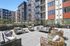Contemporary outdoor patio with stylish wicker seating, lush greenery, and modern apartment building backdrop.
