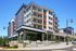 Modern multi-story apartment building with vibrant facade, featuring spacious balconies and landscaped surroundings under a clear blue sky.