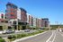 Modern apartment complex with vibrant red and gray exterior, featuring large windows and lush landscaping beside a clean, well-maintained street on a sunny day.