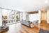 Bright and contemporary open living space with large windows and hardwood floors, featuring a cozy grey sofa and stylish decor.