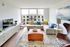 Bright and modern living room with large windows, stylish sectional sofa, and chic decor, overlooking a cityscape.