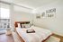 Bright and inviting bedroom featuring a modern bed with plush pillows and elegant framed wall art. Large windows bathe the space in natural light, enhancing warmth and comfort.