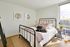 Bright and inviting bedroom with stylish iron bedframe, vibrant pillows, and large window offering city views.