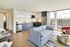 Modern apartment living room with open kitchen, featuring sleek cabinetry, stainless steel appliances, and a cozy seating area with city views.