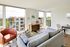 Bright and inviting living room with modern decor, featuring a cozy armchair, plush gray sofa, and large windows with a view of a stylish apartment complex.