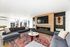 Luxurious modern living room with stylish grey sofas, vibrant red patterned rug, sleek built-in fireplace, and large windows offering city views.