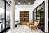 Welcoming reading nook with natural light, featuring rattan chairs, a plush armchair, and a stocked wooden bookshelf.