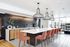 Modern kitchen featuring sleek wooden cabinetry, a spacious white island with orange chairs, and stylish pendant lighting in a bright open-concept layout.