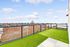 Spacious rooftop terrace with green turf and stunning panoramic views of the town and hills under a blue sky.
