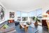 Bright and modern living room with large windows offering scenic city views, stylish gray sectional sofa, vibrant artwork, and lush indoor plants.