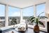 Bright and airy living space with panoramic city views, featuring large windows, cozy seating, and lush green plants.