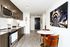 Modern kitchen featuring sleek dark cabinets, stainless steel appliances, and a chic dining area with vibrant orange chairs and a unique wall art piece.