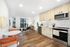 Modern open-concept kitchen and living area with sleek appliances, warm wood flooring, and abundant natural light from large windows.