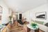 Modern open-concept living area featuring a stylish kitchen, cozy seating, vibrant artwork, and elegant wooden flooring.