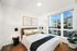 Elegant and cozy bedroom with modern decor, featuring a plush bed, stylish artwork, and a large window with urban views.