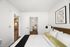 Elegant bedroom with stylish decor, featuring a comfortable bed, modern art, and a view into a sleek bathroom and kitchen area.