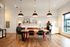 Modern open-concept kitchen with stylish lighting, spacious dining area for productivity, and contemporary finishes. Natural light fills the room through large windows creating a warm, inviting space.