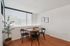 Bright dining area with modern black chairs, a round wooden table, and abundant natural light from large windows.