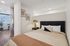 Inviting bedroom with soft lighting, modern décor, and a comfy bed, connected to an open living area with stylish furnishings.