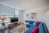 Bright and modern living room featuring a stylish blue sectional sofa, contemporary art, and a sleek TV setup with large windows showcasing natural light.
