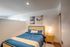 Cozy bedroom with stylish decor including blue bedding, wooden nightstand with lamp, and modern abstract wall art.