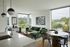 Modern apartment with a sleek kitchen, stylish green velvet sectional, and large windows offering stunning views.
