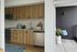 Modern kitchen with sleek wooden cabinets, stainless steel appliances, and a cozy balcony featuring stylish outdoor seating and a potted plant.
