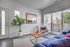 Bright and inviting living room with large windows, a cozy blue sofa, and stylish decor including a lush potted plant and modern artwork.
