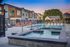 Luxurious apartment community showcasing a beautiful pool area with lounge chairs, surrounded by modern townhouses and stunning mountain views at sunset.