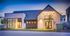 Modern apartment building with large windows and sleek design, beautifully lit during twilight with inviting entrance and impeccable landscaping.