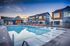 Luxurious apartment complex featuring a pristine swimming pool with sun loungers, modern architecture, and a scenic sunset backdrop.