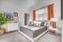 Bright and cozy bedroom with a modern design, featuring a plush bed, stylish artwork, rich orange curtains, and elegant decor.