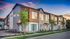 Charming modern townhouses with large windows, surrounded by lush landscaping and set against a vibrant sunset sky, offering a serene and stylish living environment.