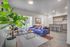 Chic modern living room with vibrant blue sofa, lush indoor plant, and sleek open-concept kitchen.
