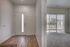 Inviting apartment entrance with elegant wood flooring, leading to bright, carpeted room with large sunlit windows overlooking a serene street view.
