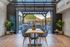 Modern indoor-outdoor dining space featuring a stylish wooden table with chic black chairs, open glass doors revealing scenic mountain views, and inviting greenery accents.