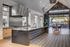 Modern kitchen with a sleek black island, stainless steel hood, and open-concept dining area leading to a patio with barbecue grills.