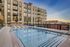 Modern urban apartment building with a luxurious pool, featuring inviting poolside loungers and stylish balconies at sunset.